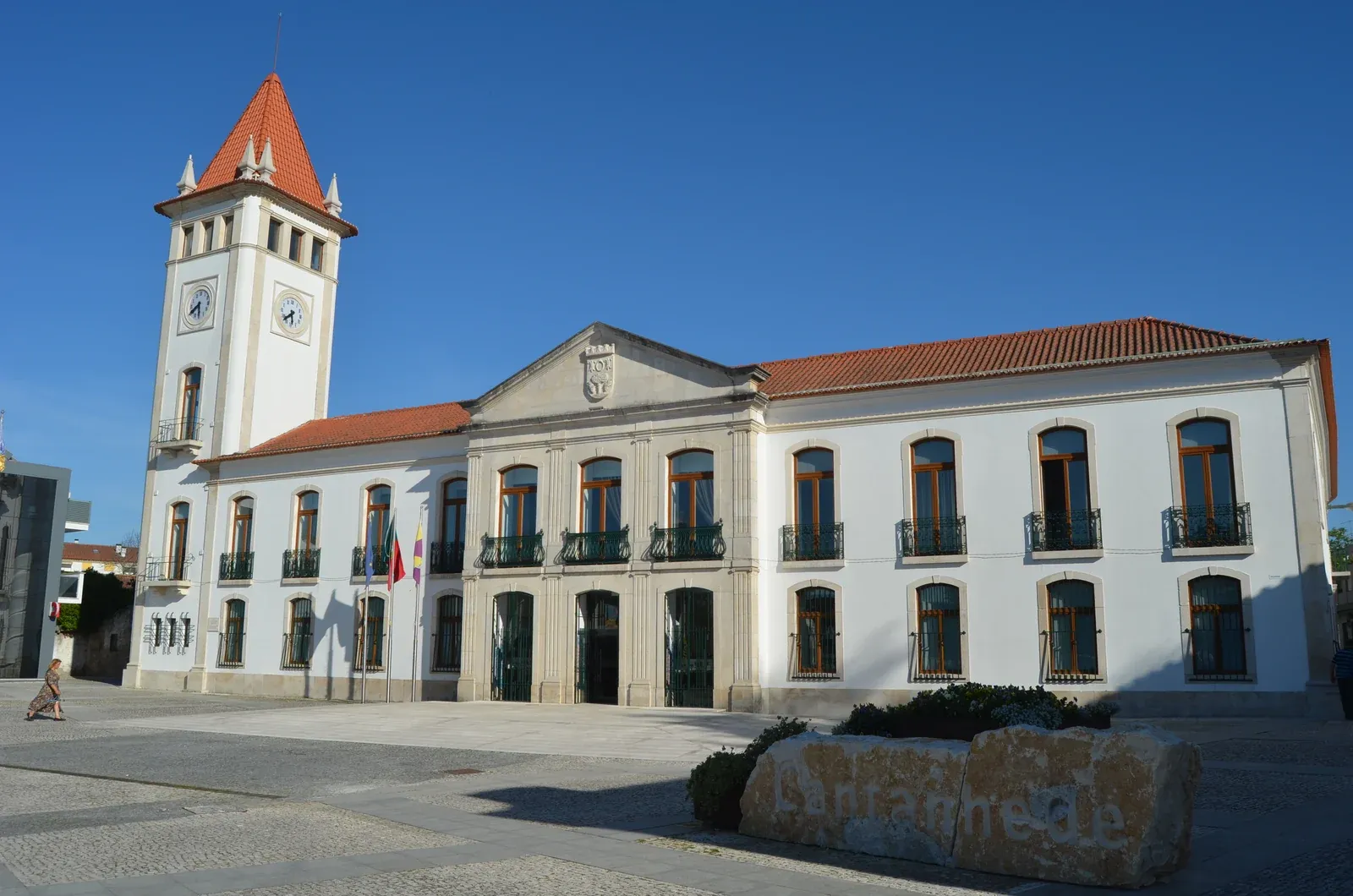 Fachada clara da Câmara Municipal de Cantanhede, com torre do relógio, varandas e praça sob céu azul